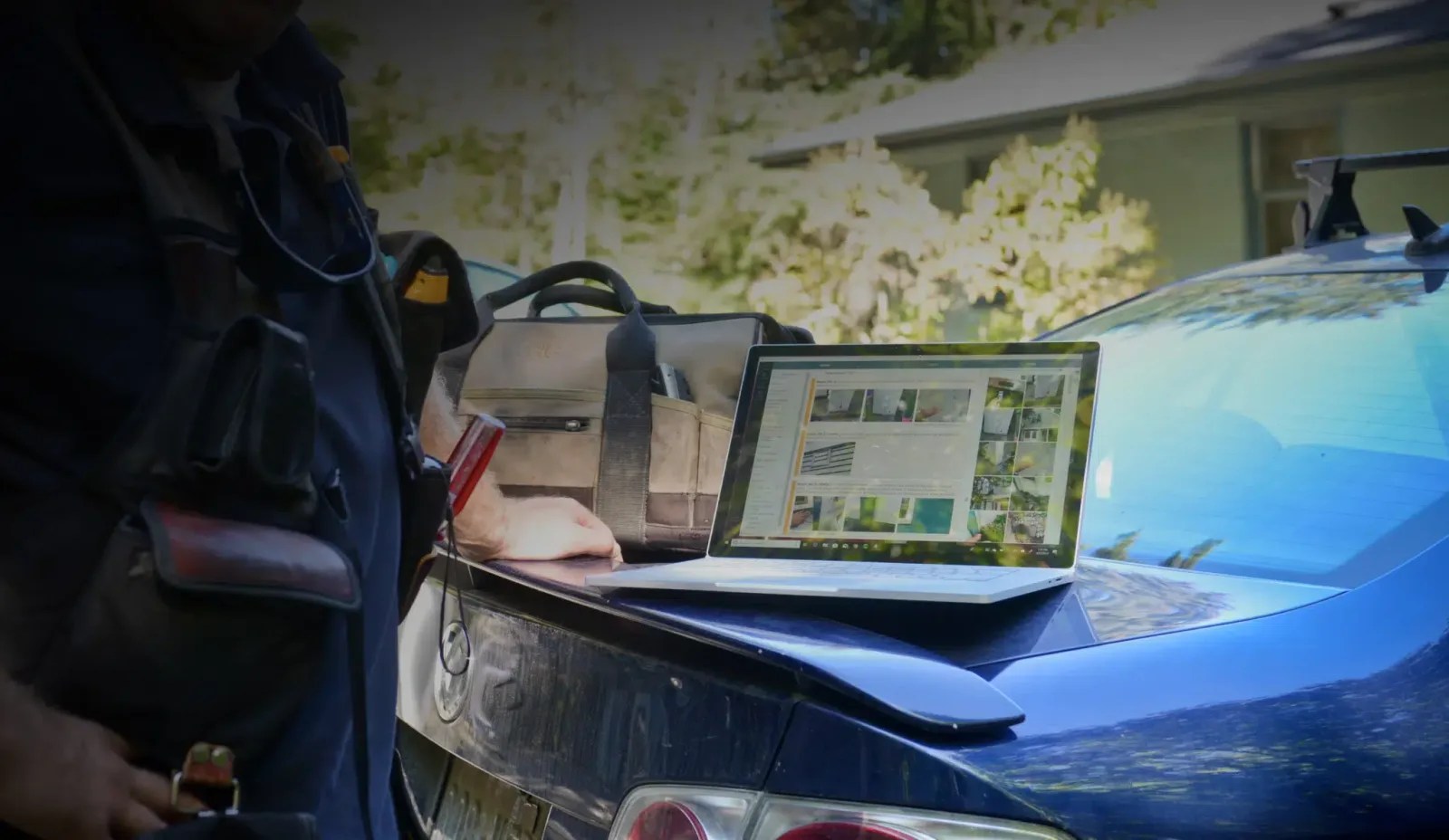 A home inspector's laptop showing a ScribeWare report, resting on a car parked outside a house during a home inspection